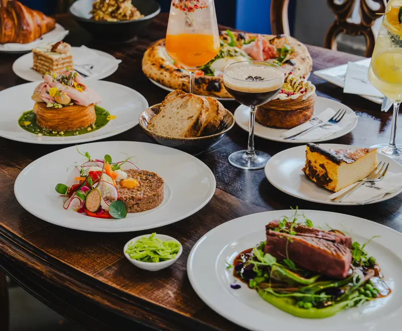 Megterített hosszú asztal croissant-nal, tatárral és koktélokkal